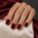 Burgundy velvet-effect bow and heart nails worn on a hand holding an ivory clutch