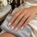 Silver glitter almond nails worn with silver satin clutch and cream dress